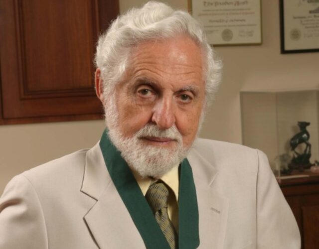 Djerassi wears a tan suit jacket and green ribboned medal around his neck